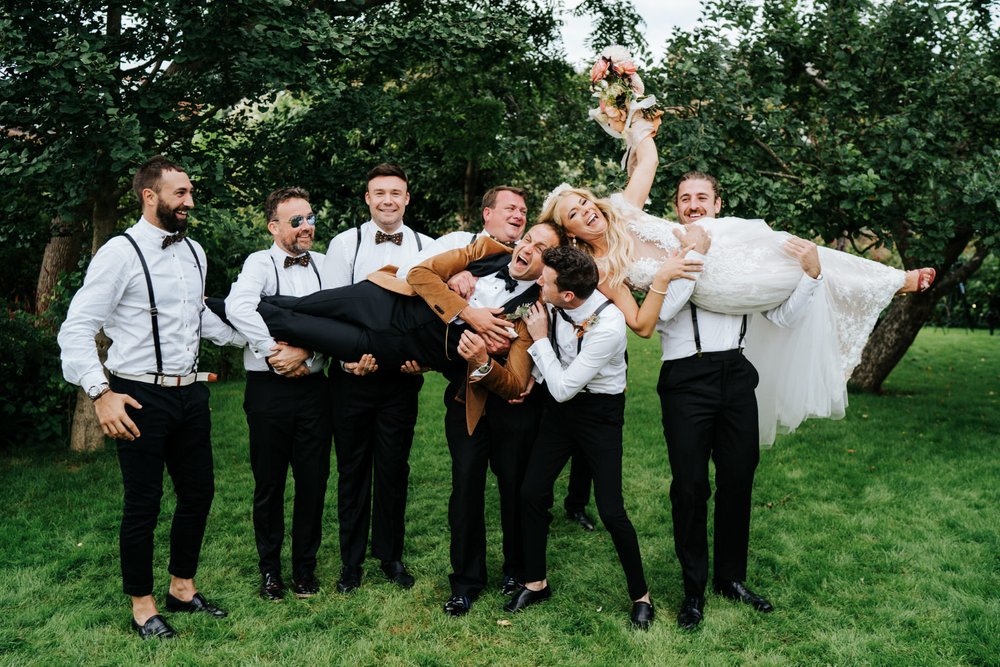 Groomsmen carry bride and groom in fun wedding photo idea at The Secret Garden in Twickenham