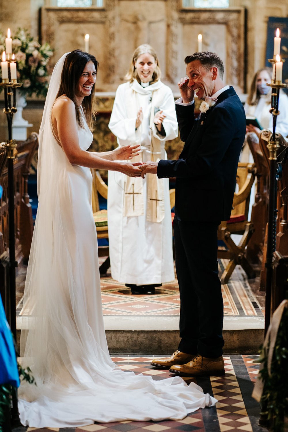 Bride and groom stand at the front of the aisle during Church of England wedding ceremony while groom dries a tear off his eye