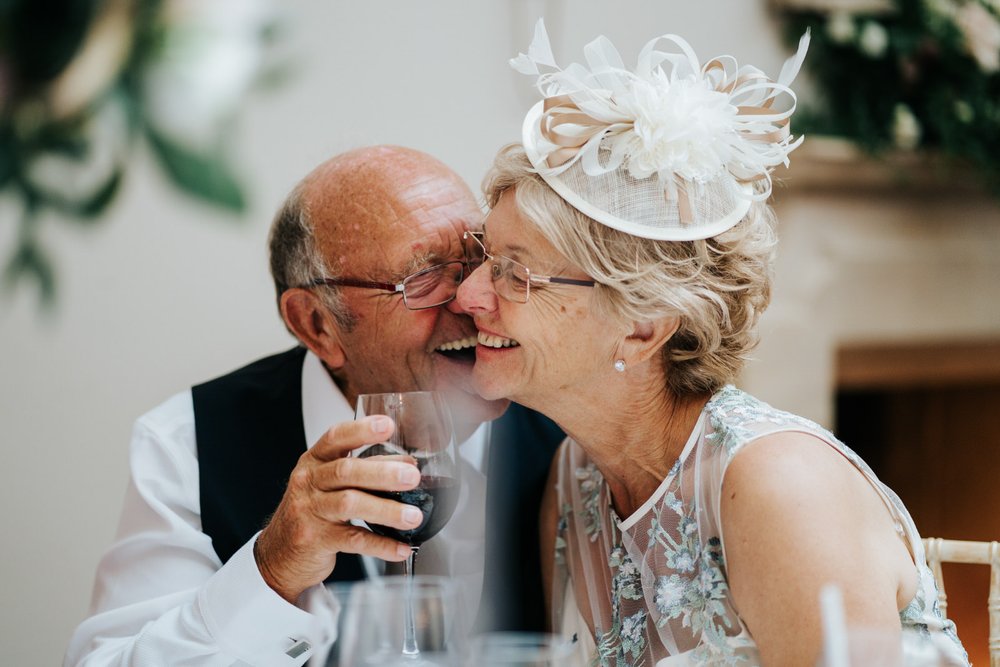 Two guests embrace as they are sat at the table during wedding reception in candid photograph taken at Foxhill Manor