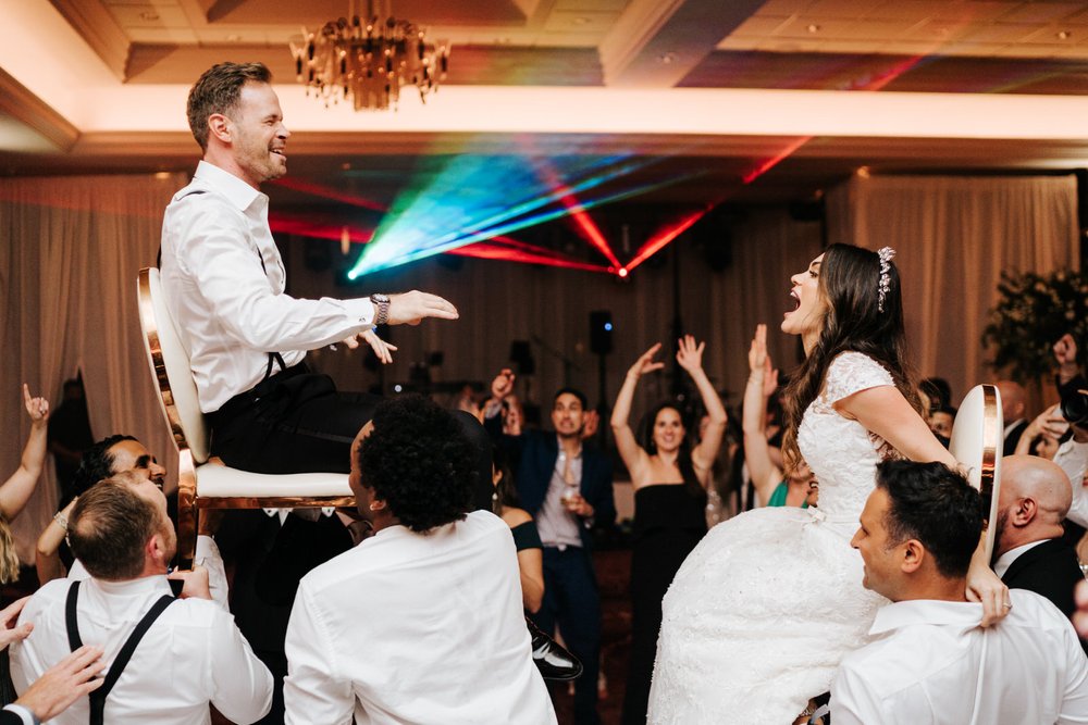 Bride and groom are hoisted on chairs during crazy wedding party while lasers go off in the background
