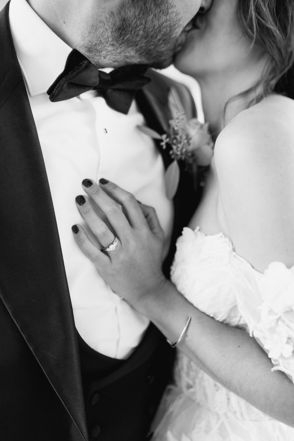 Close-up photograph of bride's left hand and wedding rings resting on groom's torso