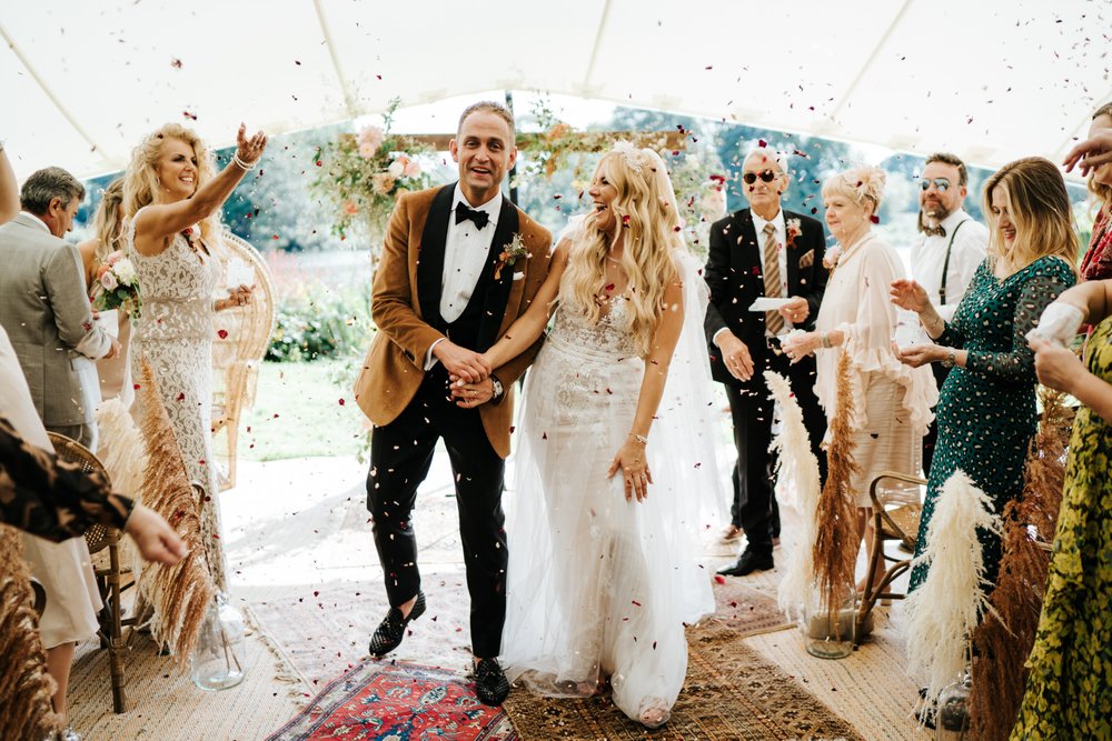 Bride and groom walk back down the aisle as married couple and are pelted with confetti at Secret River Garden Twickenham wedding