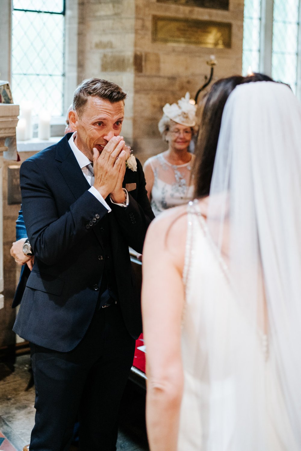 Groom, standing at the front of the aisle during Cotswolds Church wedding, cannot believe how beautiful bride looks 