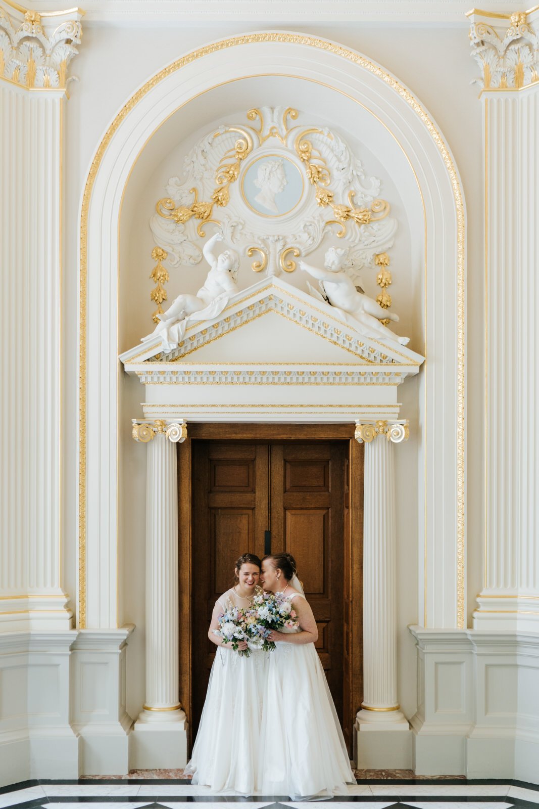 Two brides pose for photograph in dresses and floral bouquets at Orleans House Gallery wedding