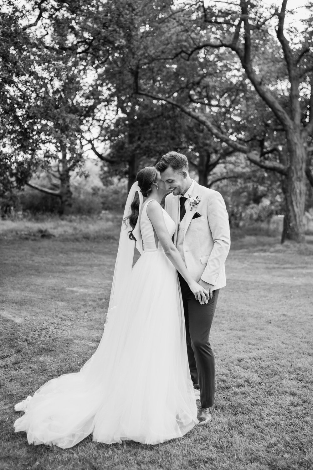 Bride and groom pose for elegant black and white wedding portrait as groom rests his forehead on bride's