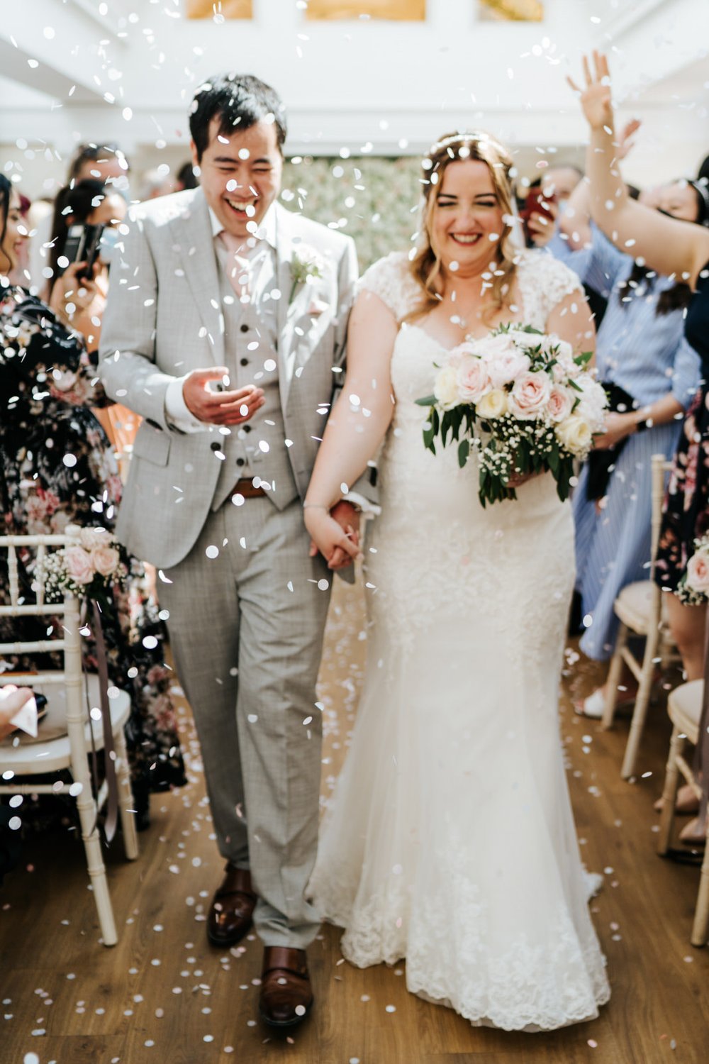 Bride and groom, out of focus, walk back down the aisle at Pembroke Lodge in Richmond Park as guests throw confetti at them 