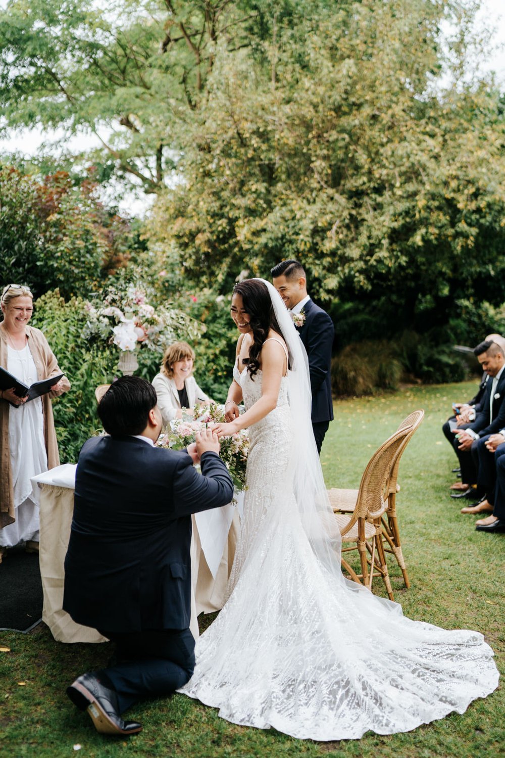 Bride smiles as best man gives her wedding ring while kneeling during wedding ceremony at Bingham Riverhouse in Richmond