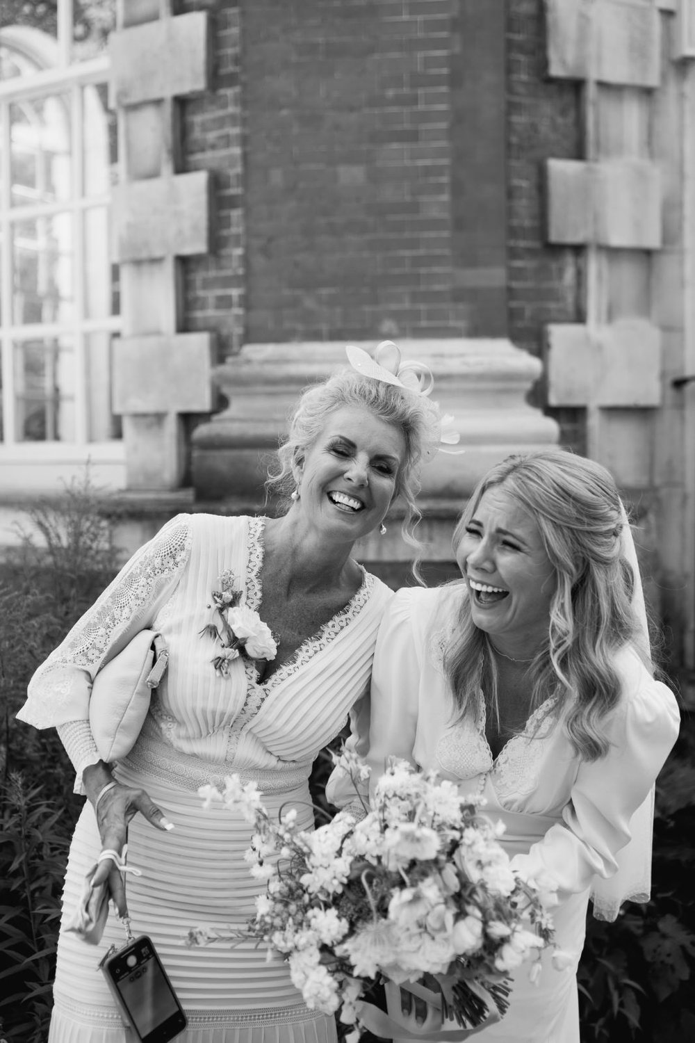 Bride and her mother laugh in candid black and white photograph 