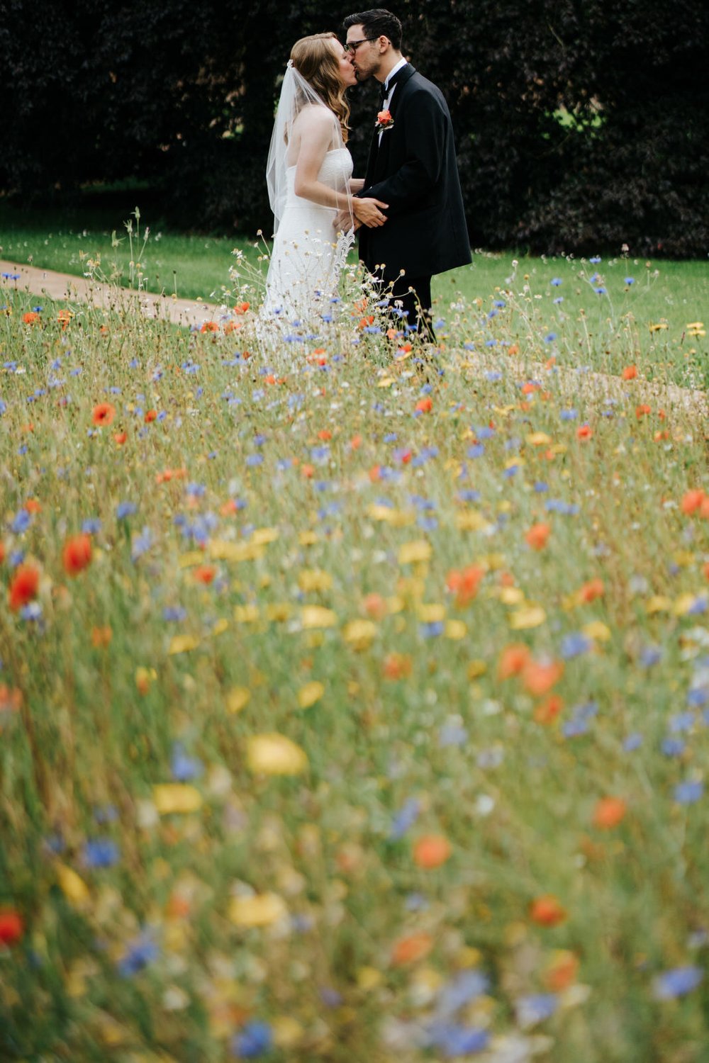Bride and groom pose behind field of wildflowers at Jesus College in Cambridge