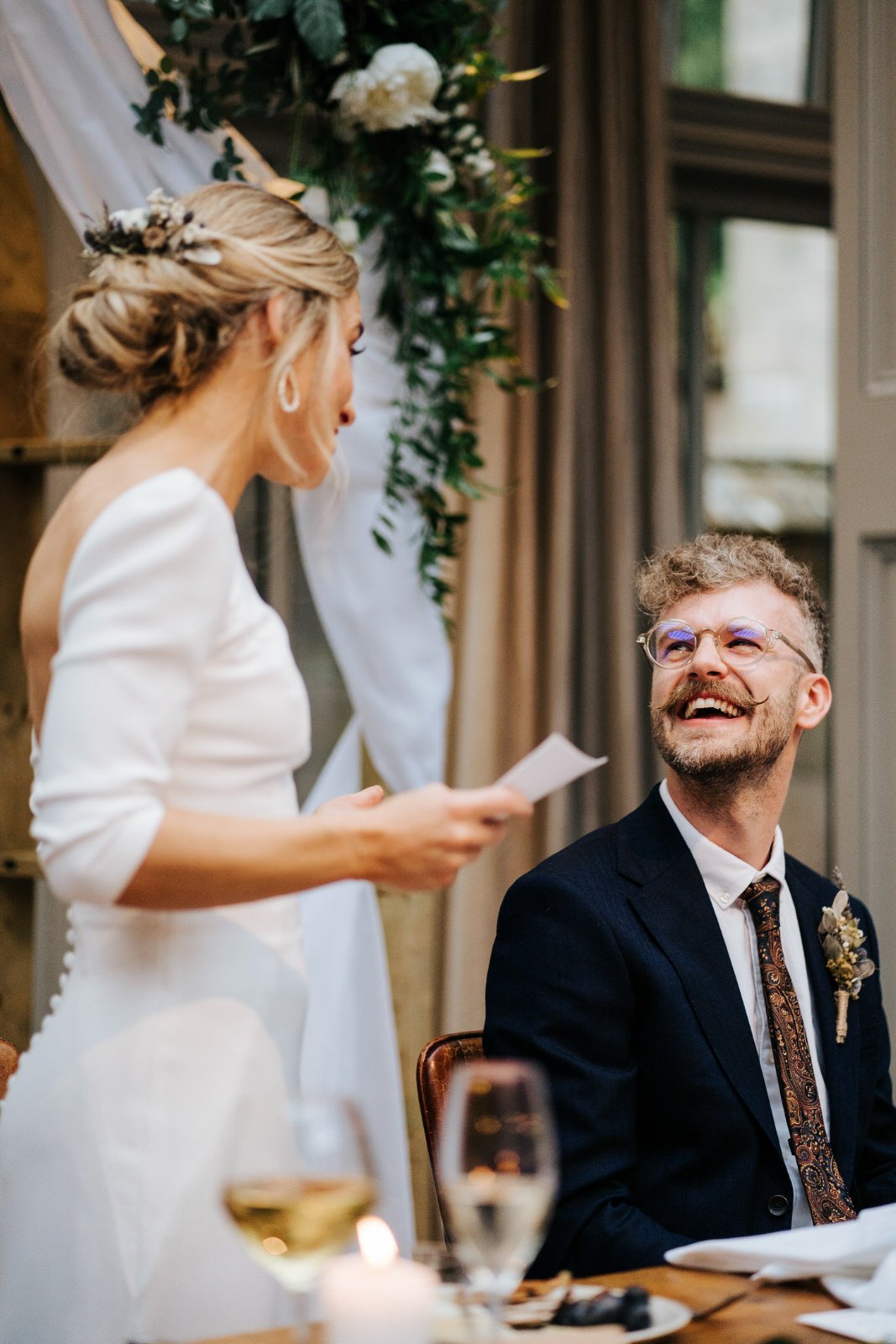 Groom smiles at his wife as she delivers wedding speech at Hampton Manor in Arden 