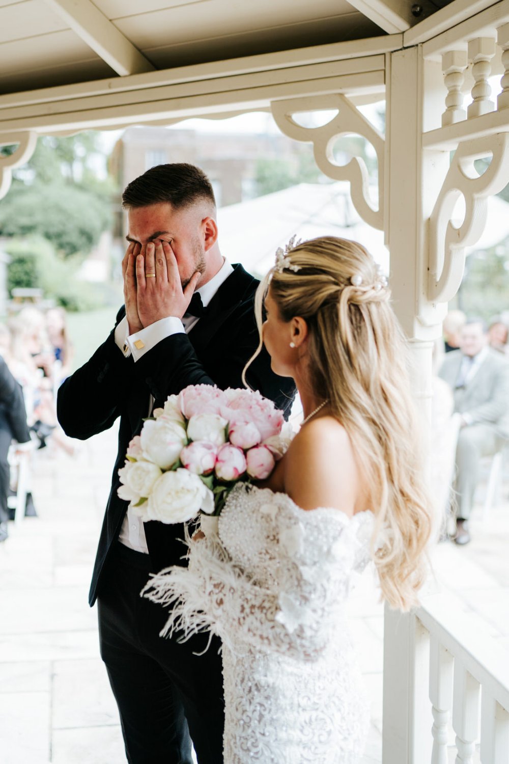 Groom covers his face while he cries after seeing bride in her wedding dress for the first time