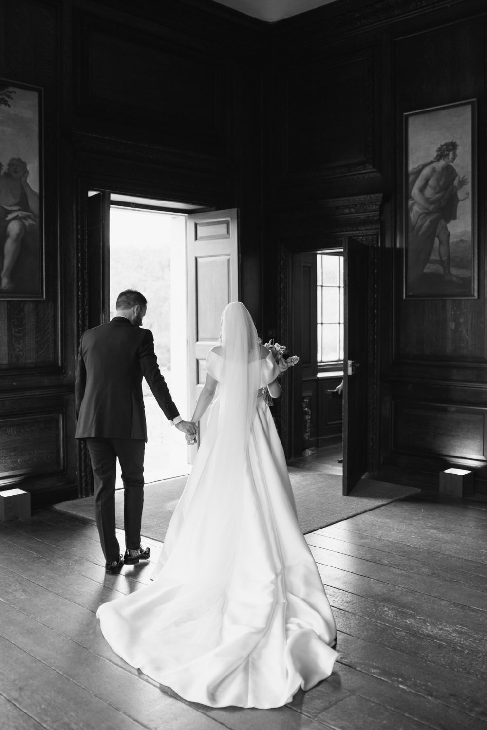 Black and white back of bride and groom as they exit Little Banqueting House in London and bride's Eva Lendel dress trails