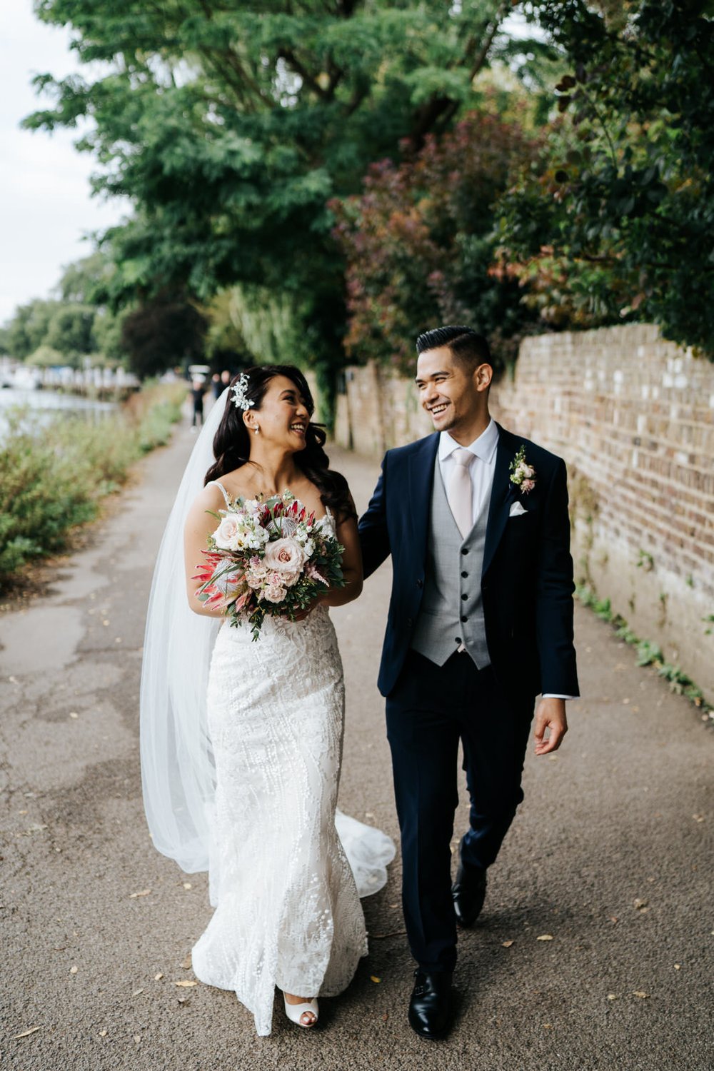 Bride and groom walk through Richmond riverside while bride holds King Protea bouquet by Johanna Pedrick Flowers