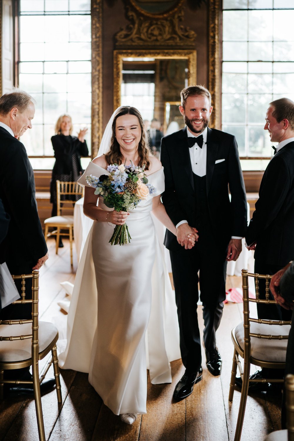 Bride and groom walk back down the aisle at Little Banqueting House wedding at Hampton Court Palace while bride holds blue bouquet 