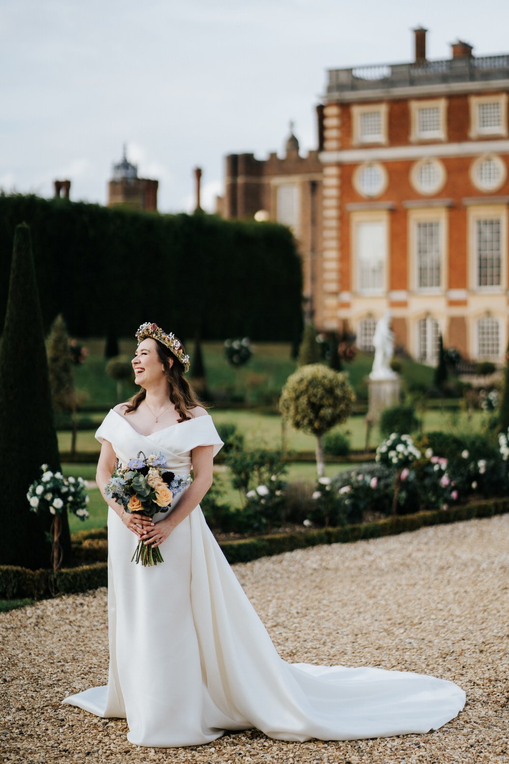 Bride in Ukrainian flower crown and flowers by My Table Floral Design poses in front of Hampton Court Palace during wedding