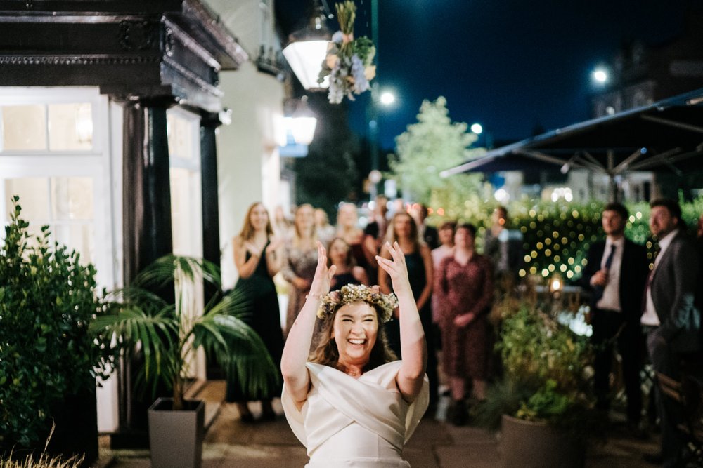 Bride smiles full of joy as she throws bouquet at friends standing behind her