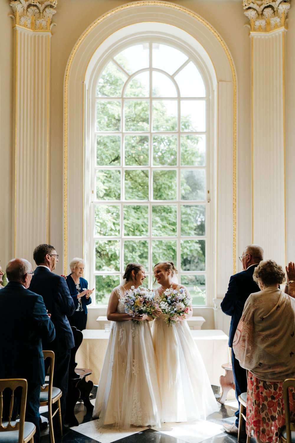 Two brides walk back down the aisle at Orleans House Gallery while holding colourful bouquets by Jessica Eliza Flowers 