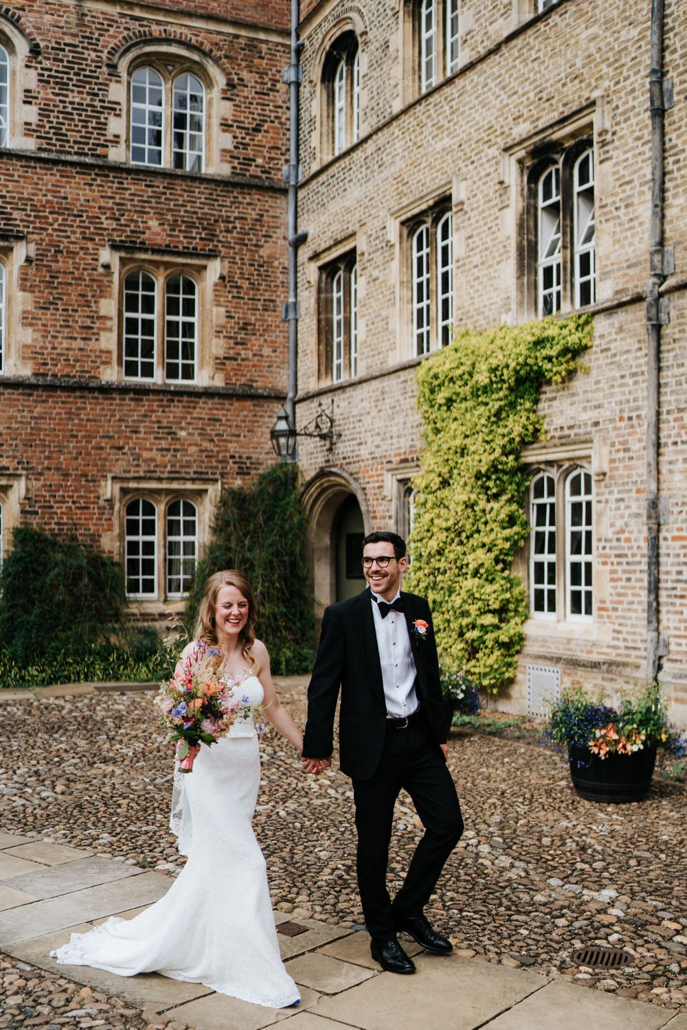 Bride and groom walk through the grounds of Jesus College in Cambridge while bride holds her beautiful wedding bouquet by Wild Rosamund