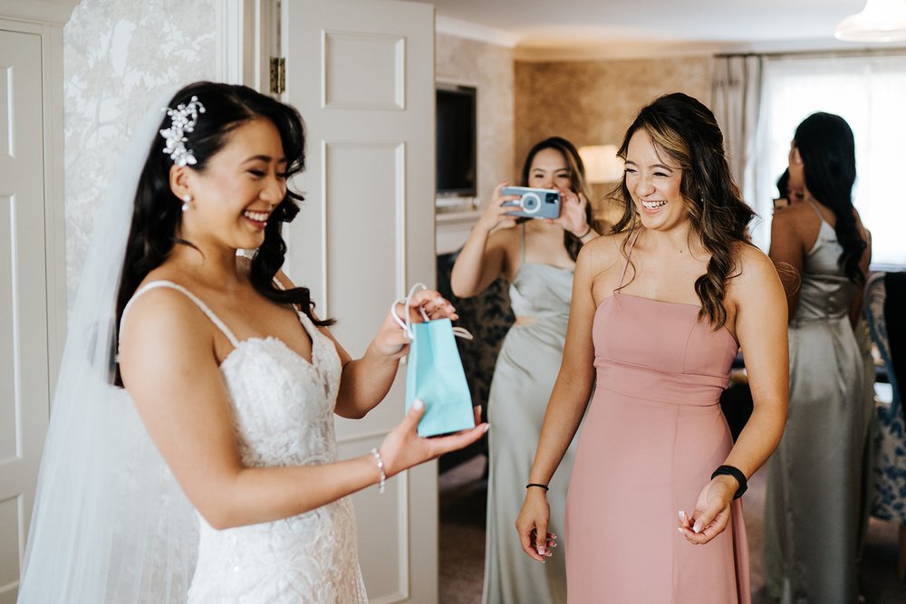 Bride in wedding gown holds Tiffany bag and smiles as she anticipates the gift she is about to receive