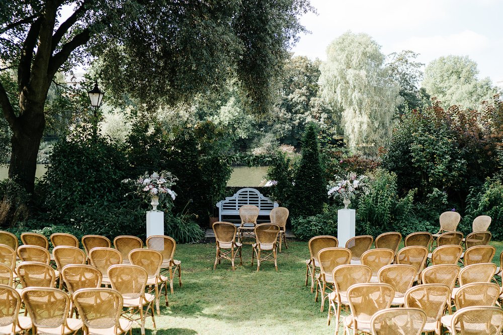 Wide photograph of outdoor ceremony setup at Bingham Riverhouse with rattan chairs and beautiful flowers by Johanna Pedrick
