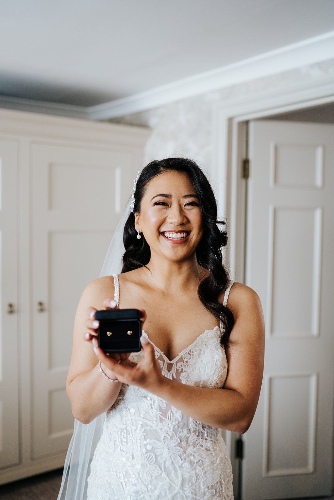 Bride stands and smiles at camera and holds open beautiful Tiffanys gift that groom gave her on wedding day