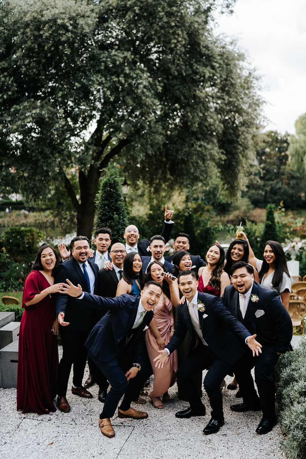 Groom and group of friends cheer for group photo with lush green foliage and thames river in the background