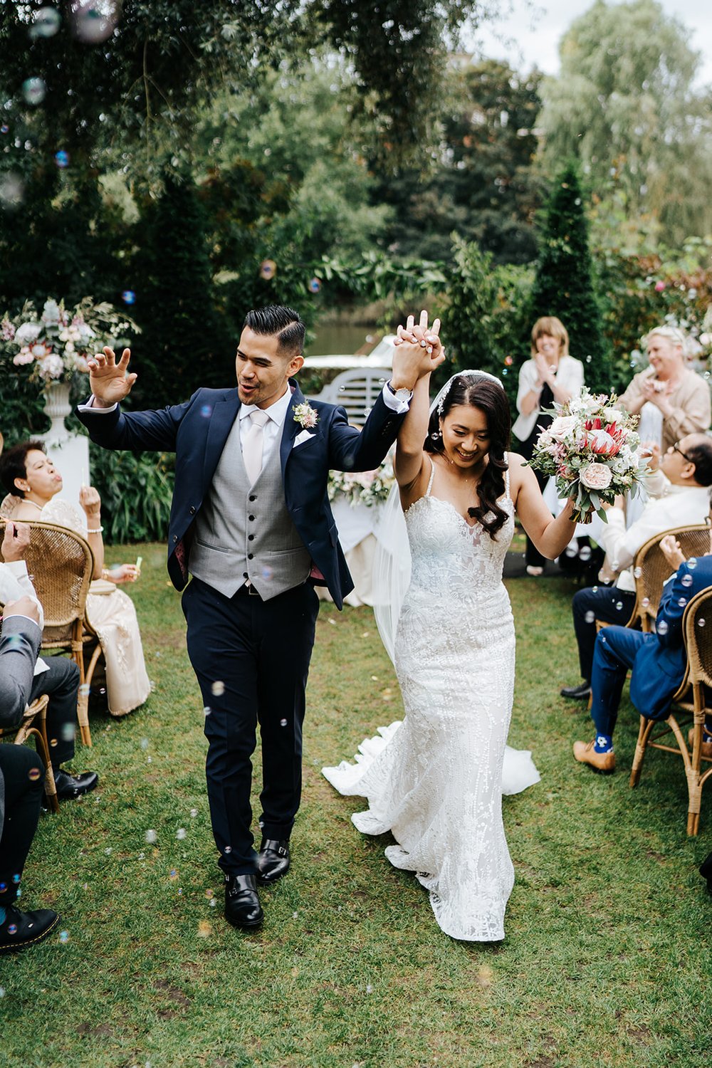 Bride and groom walk back down the aisle holding hands and cheering with fists up in the air