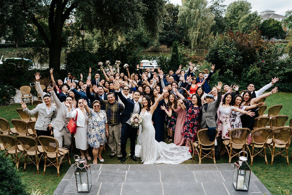Wide group shot of bride, groom and all their guests cheering and looking at camera after outdoor ceremony in Richmond Bingham Riverhouse