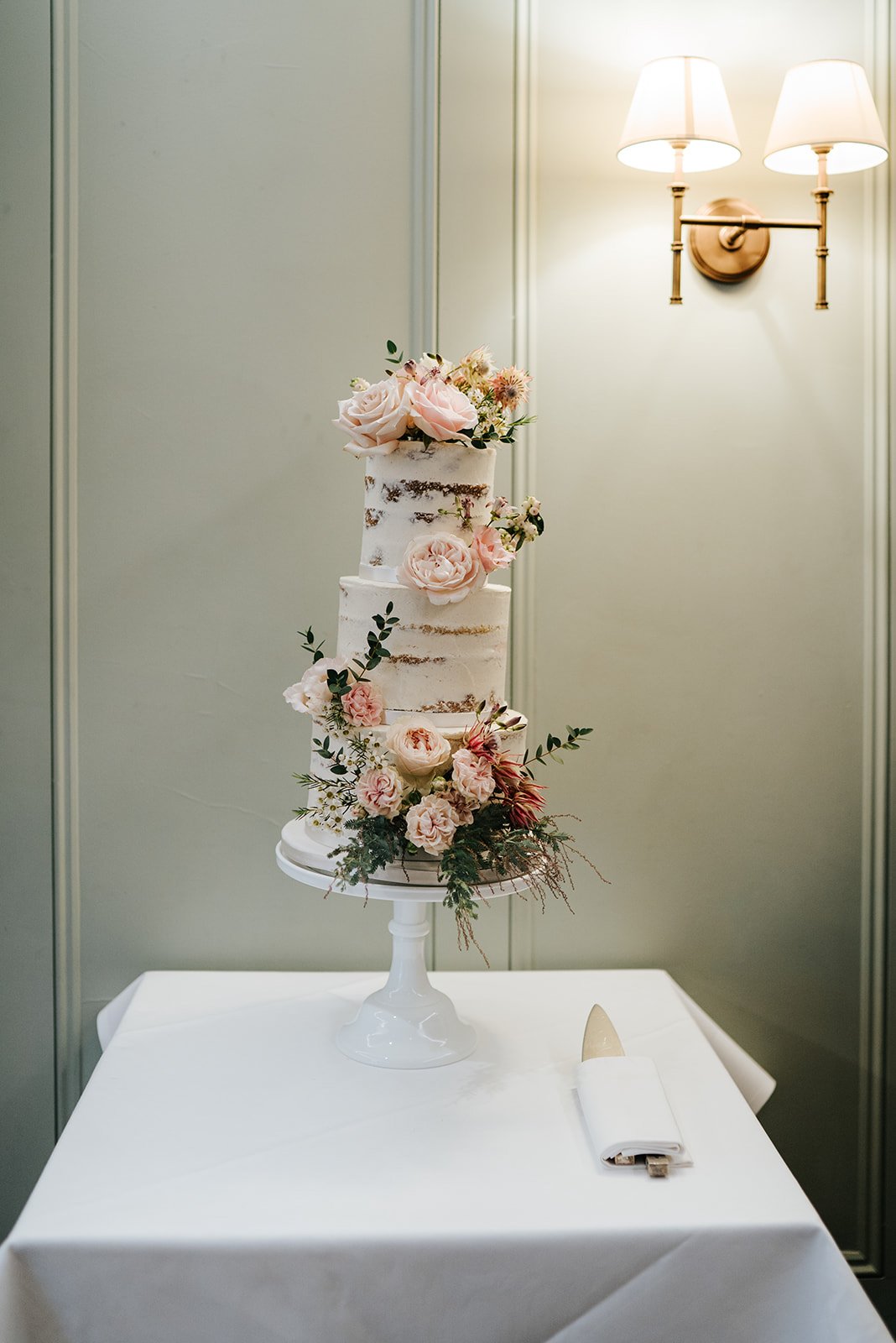 Three tier white wedding cake decorated with pastel coloured flowers and green foliage