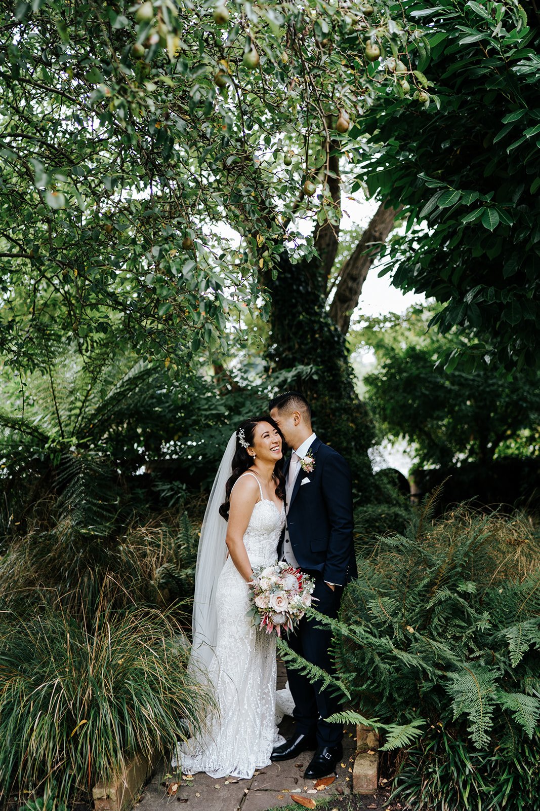 Bride and groom pose and cuddle in green, foliage heavy photograph