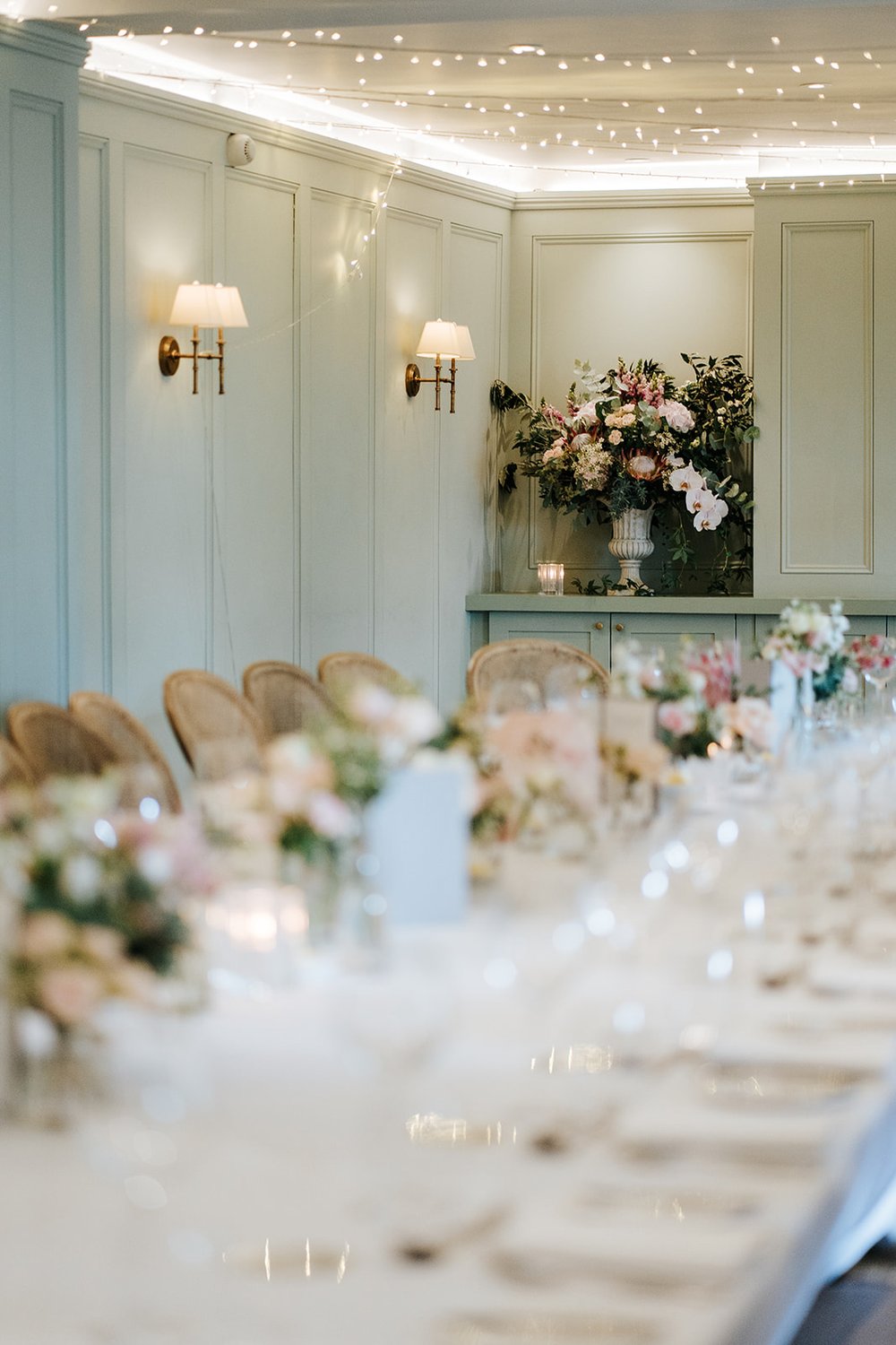 Photograph of long table for wedding breakfast setup with lovely flowers by Johanna Pedrick. The tones are pastel, muted and mostly green and blue hues