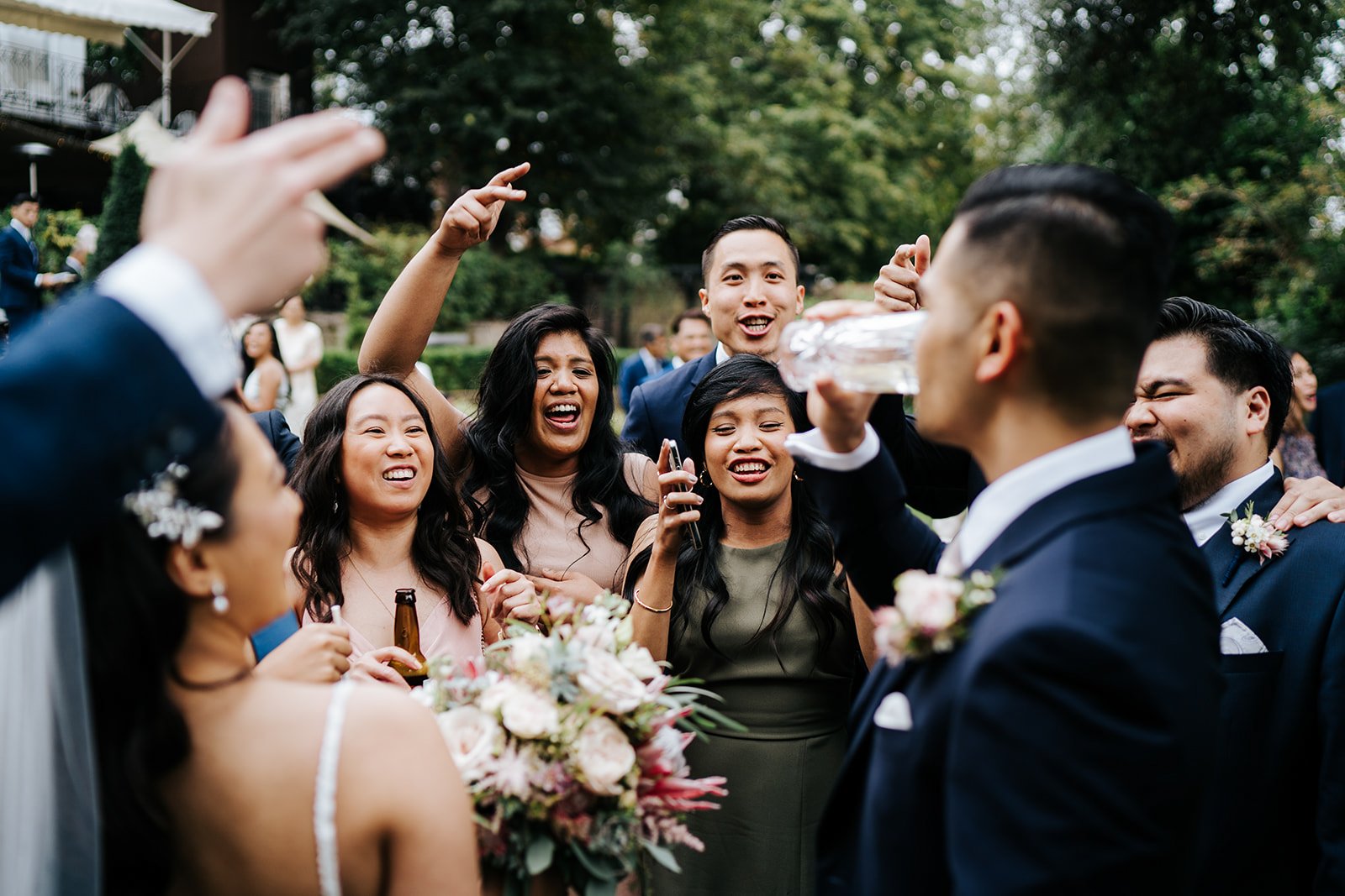 Groom and a group of 20 friends jump and cheer during cocktail hour as groom takes a shot of alcohol