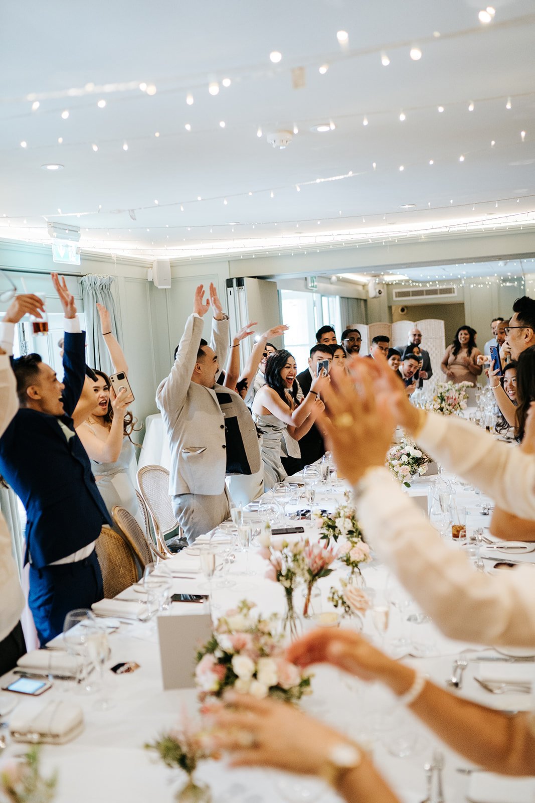 Excited guests stand up from their seats to make mexican wave as bride and groom enter the wedding breakfast room 