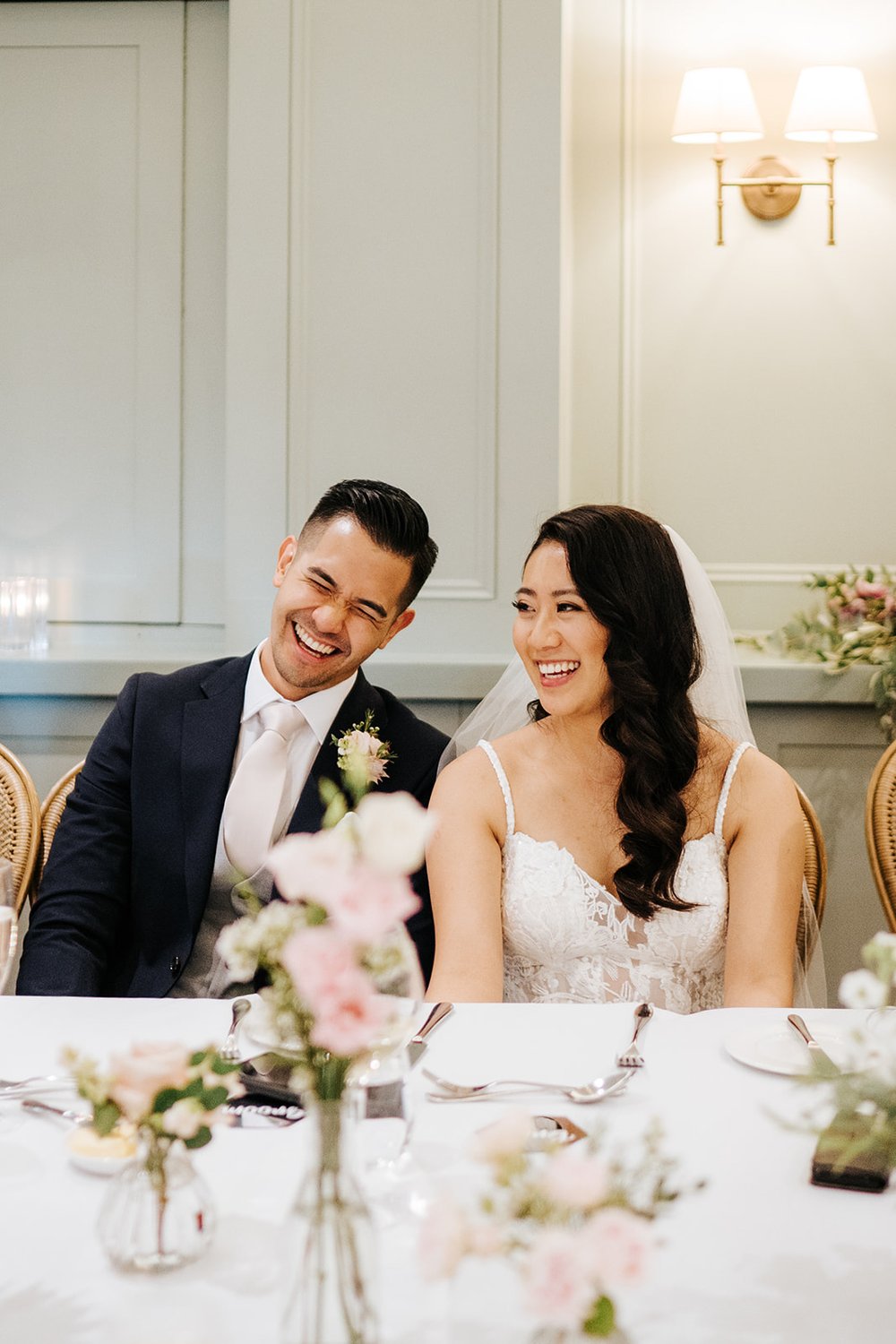 Close-up photo of bride and groom sat down during speeches and smiling