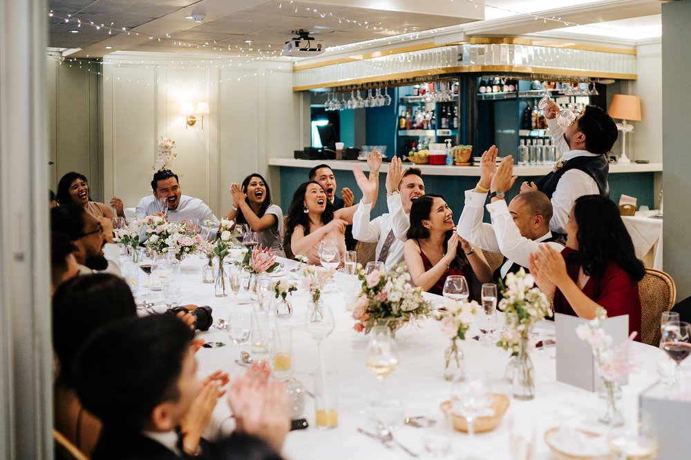 Wide photograph of guests clapping and cheering as best man wraps up his wedding speech at Bingham Riverhouse wedding