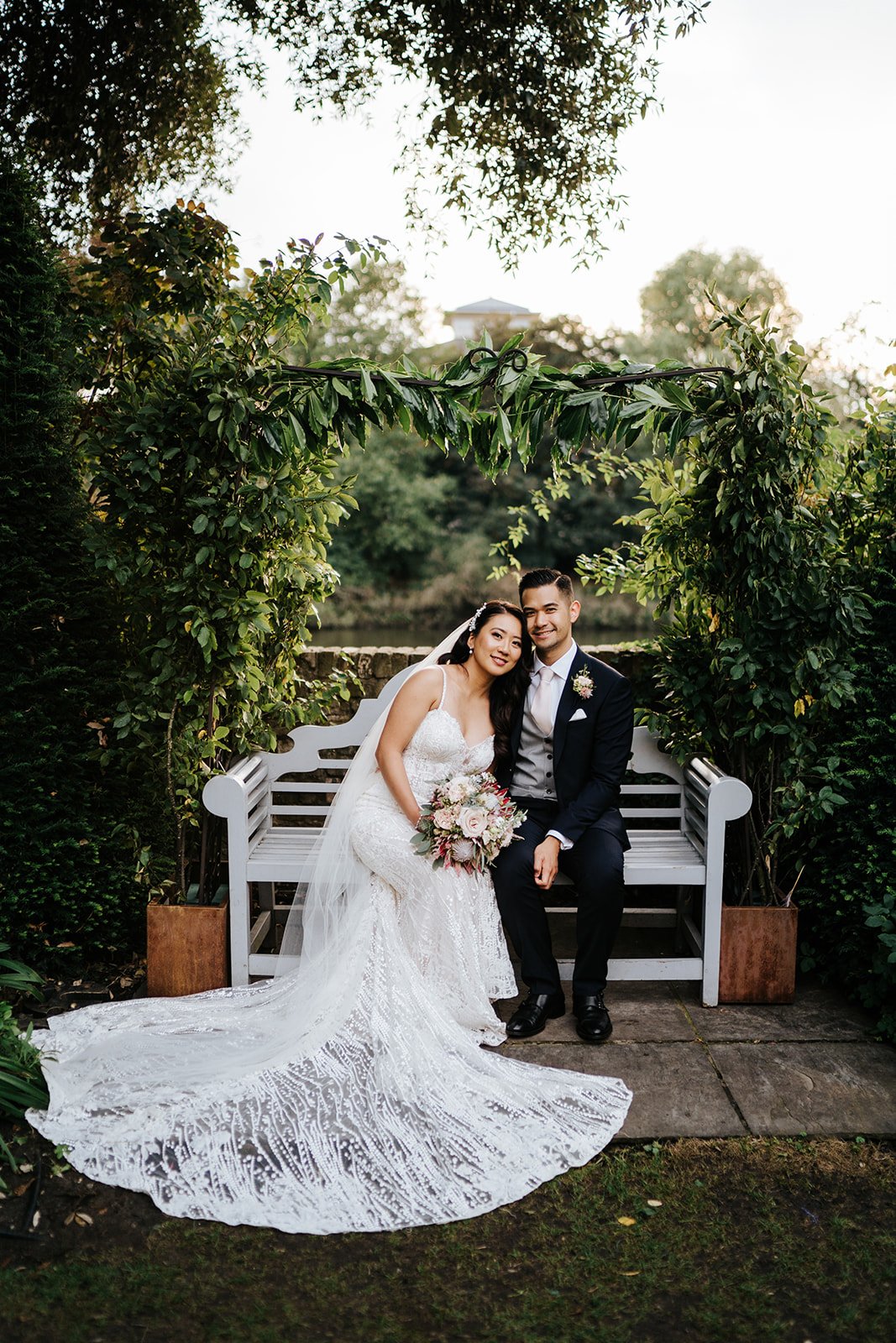 Bride and groom sit on romantic bench at Bingham Riverhouse with Thames in the background