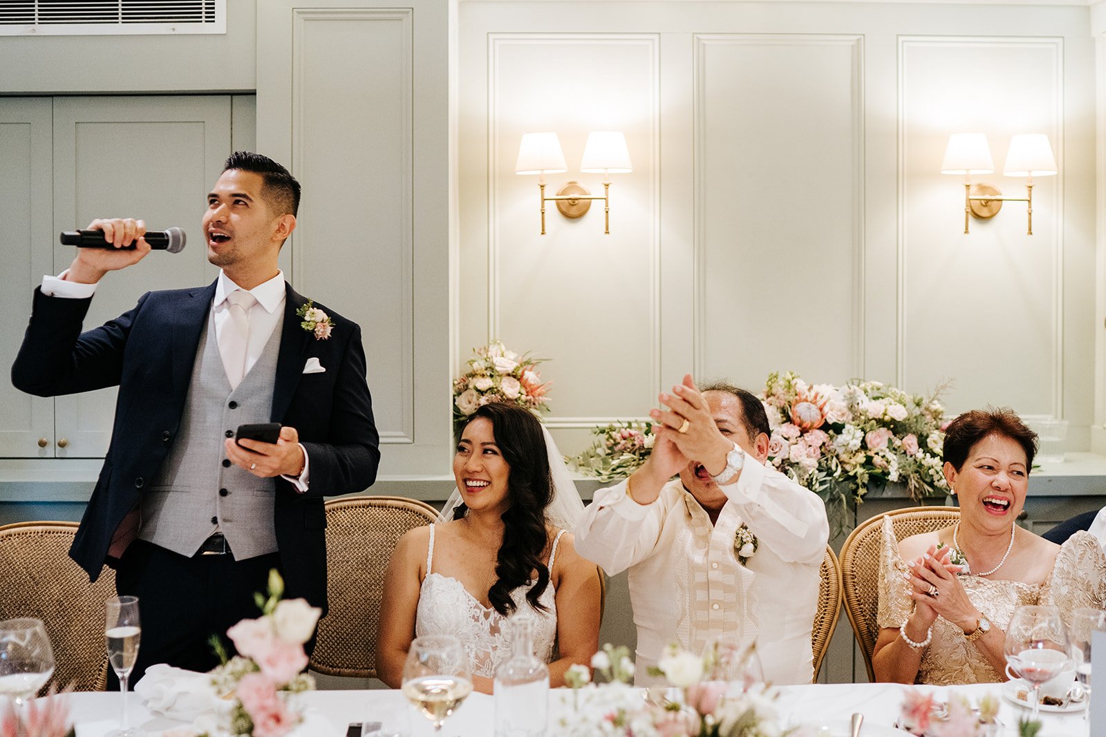 Groom continues delivering wedding speech to everyone's enjoyment while father of the bride claps and cheers