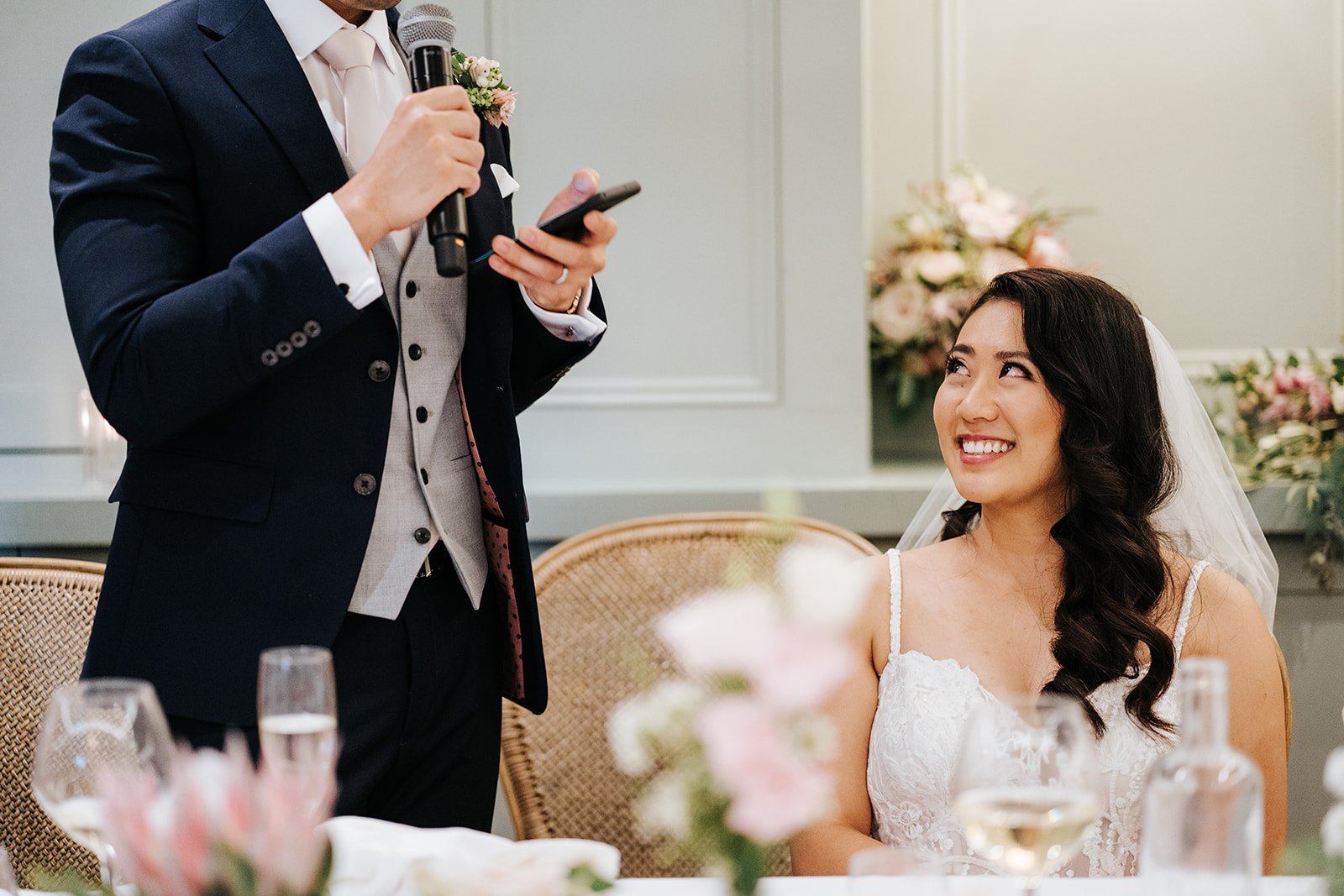 Groom, slightly cut out, delivers loving and romantic words to bride, sat down, during his wedding speech