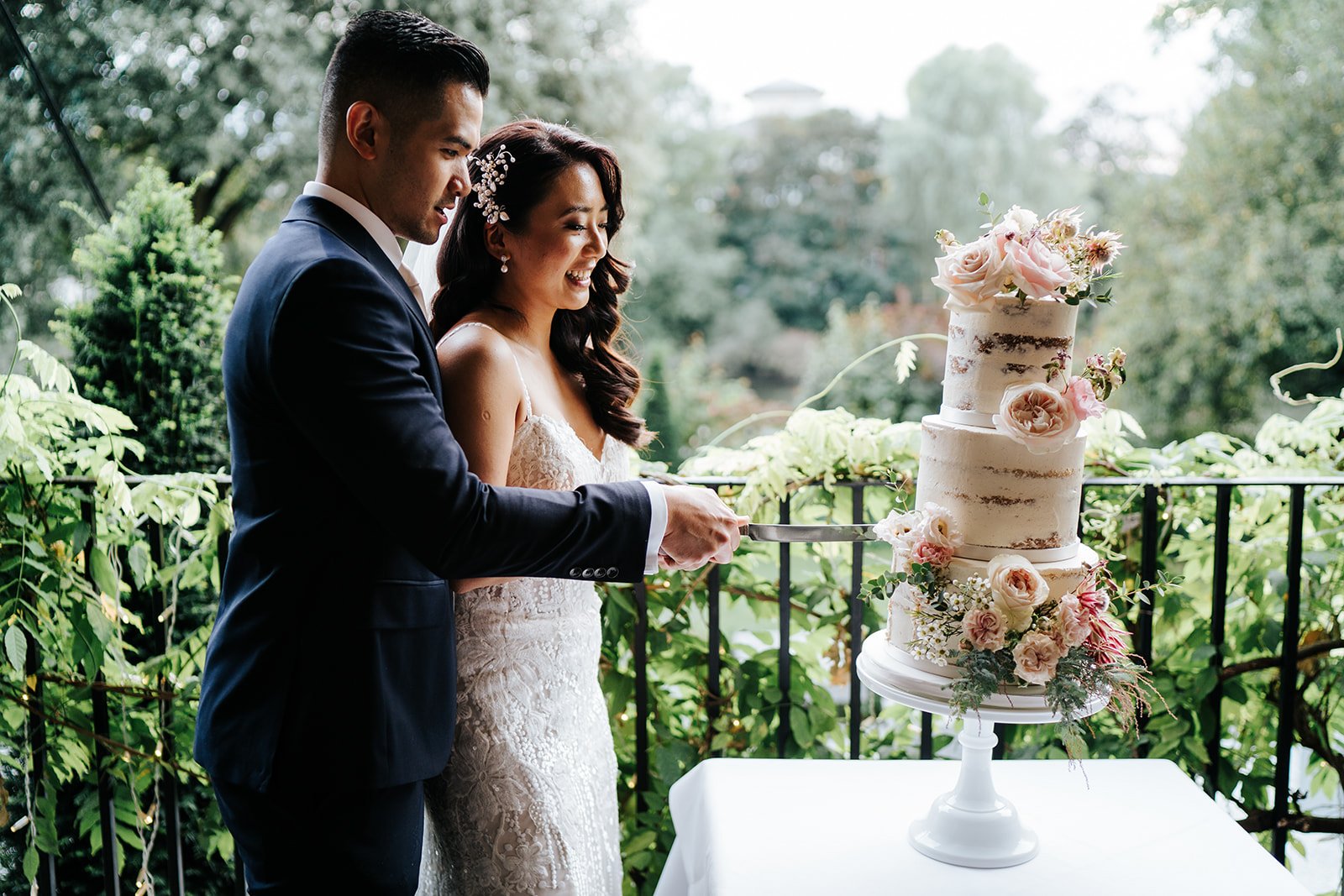 Bride and groom stand and cut wedding cake in Bingham Riverhouse gardens in dimly lit photograph