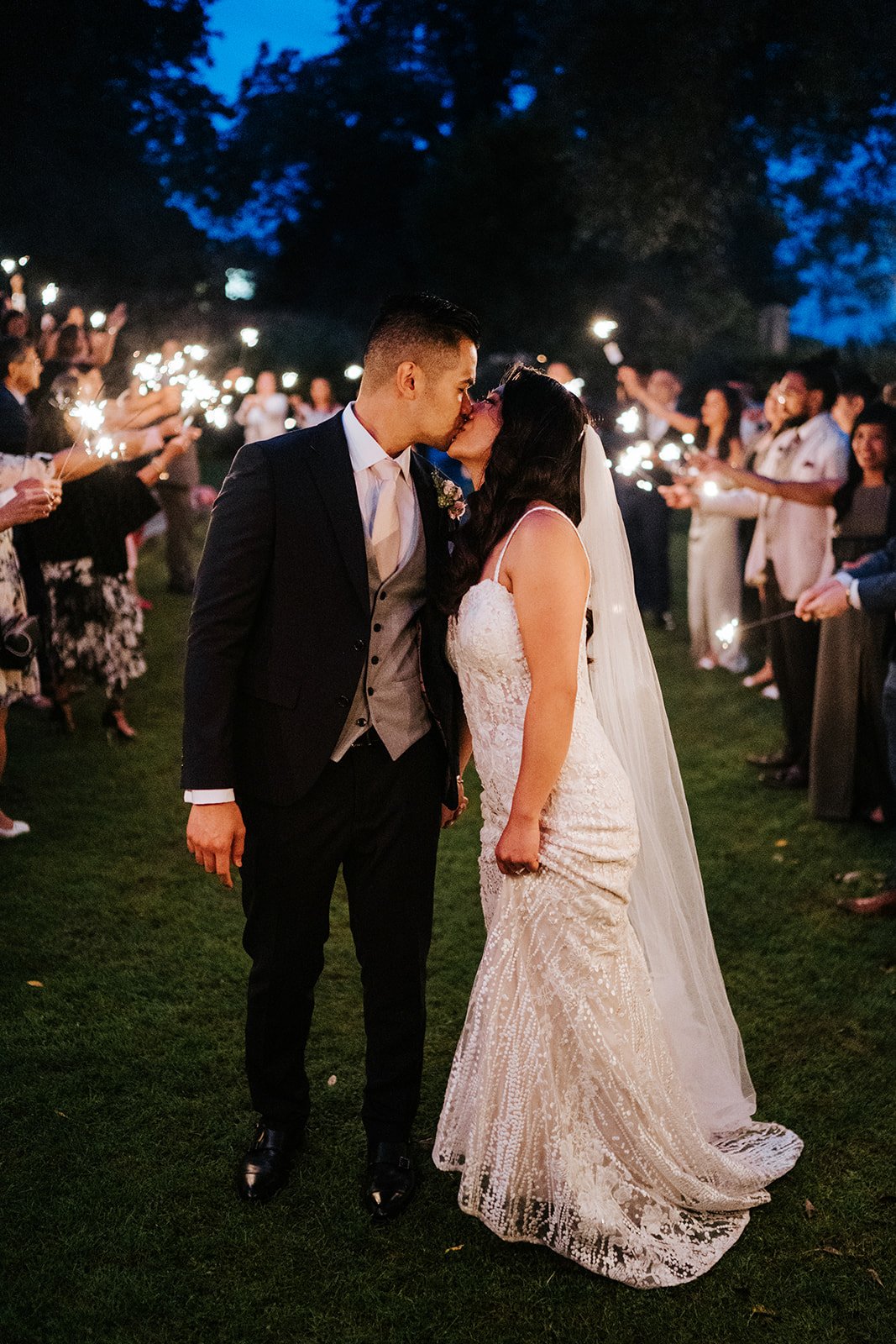 Bride and groom share a kiss as they walk down tunnel of sparklers held by guests 