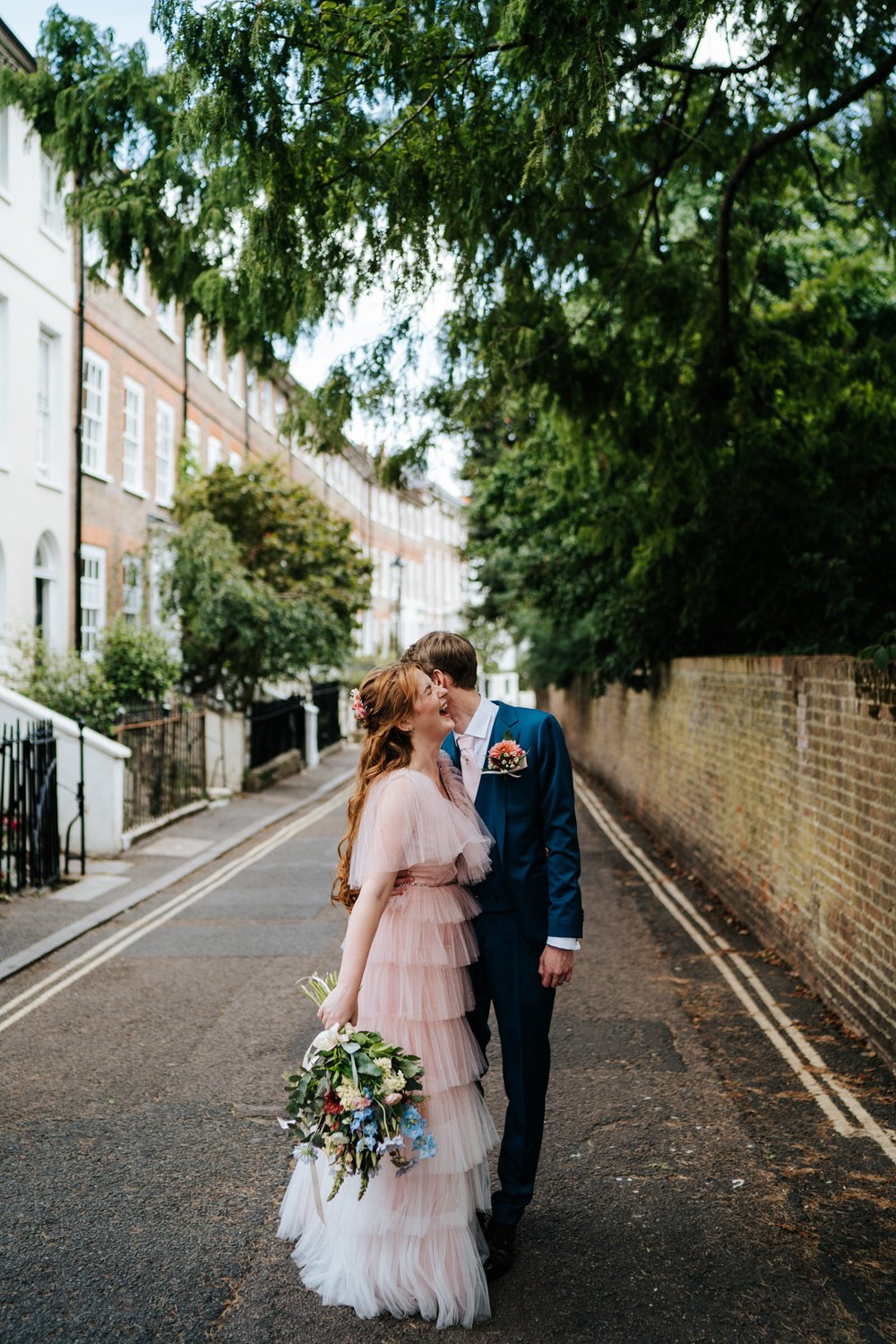 Groom whispers something in ear of bride wearing pink dress as she reacts with laughter in gorgeous York House wedding photograph