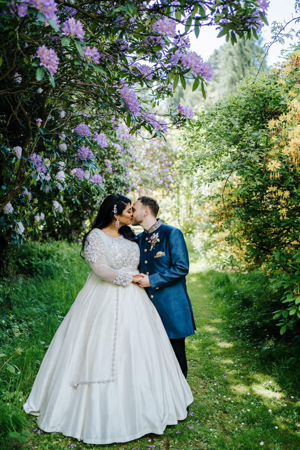 Bride and groom pose under beautiful, violet flowers at Walcot Hall wedding