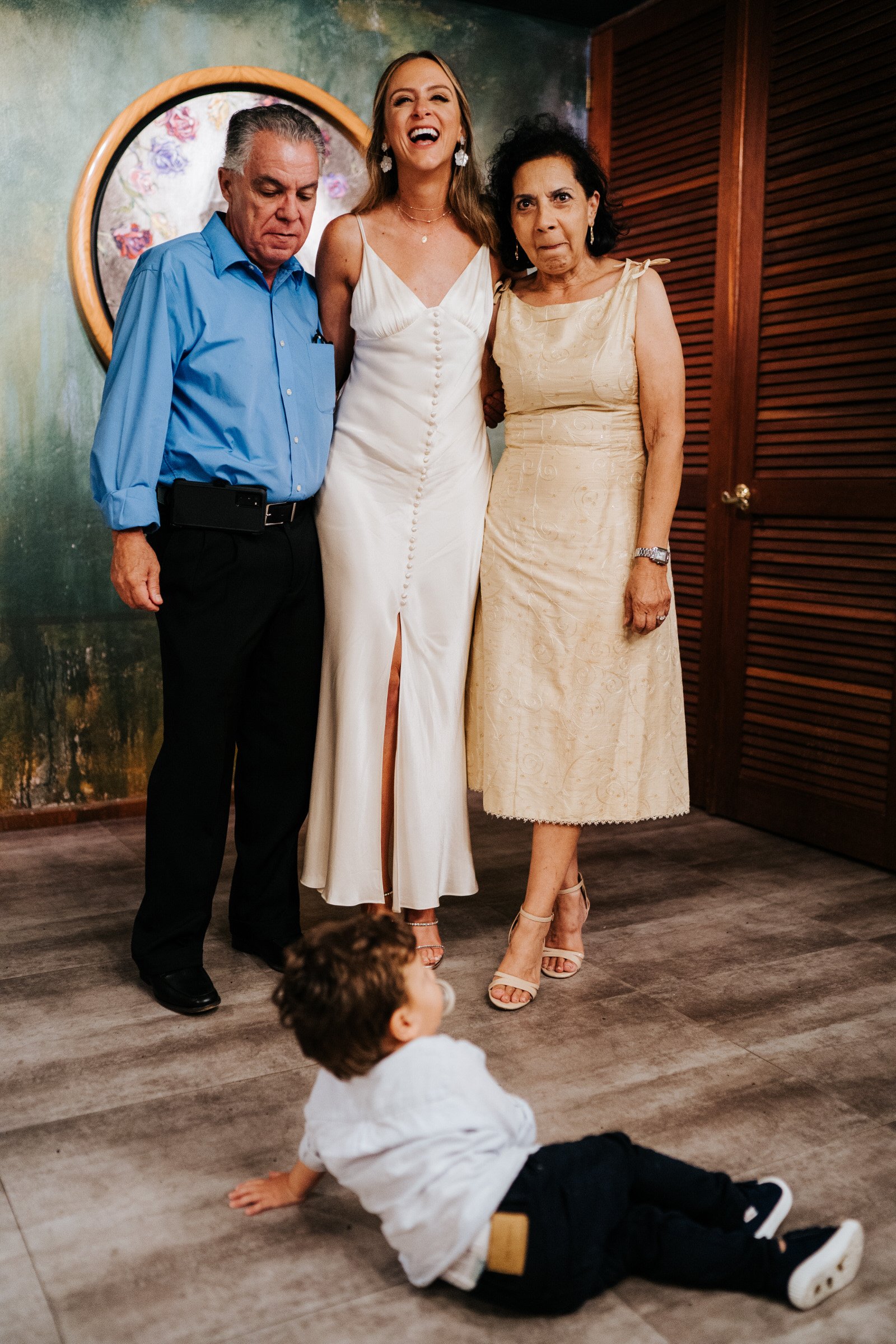 Little boy throws himself onto the ground as bride has her photograph taken with her parents. Bride is seen smiling at Puerto Rico El Convento wedding