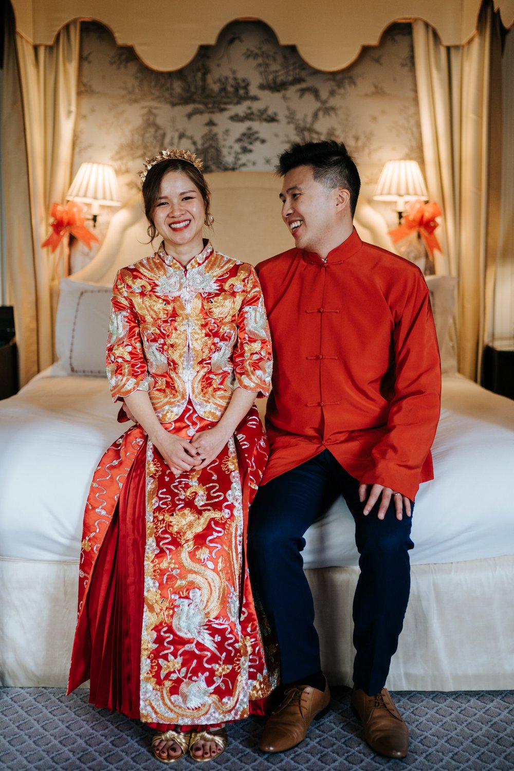 Bride and groom, in beautiful red Chinese dress, pose for photograph on top of bed