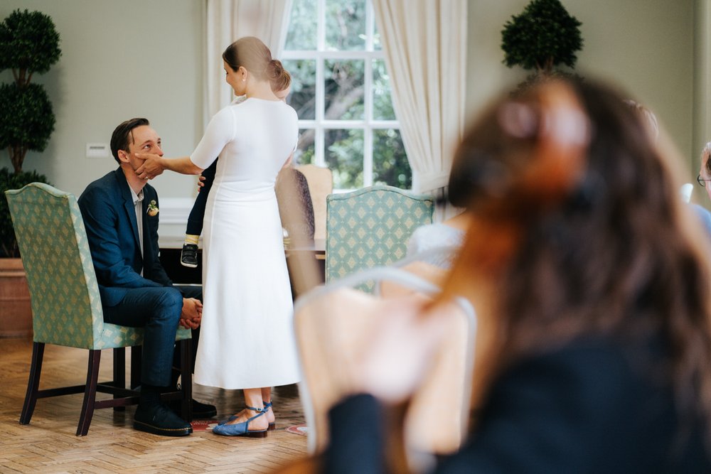 Bride gently caresses groom's check as she holds her son and a friend plays the violin during York House wedding ceremony