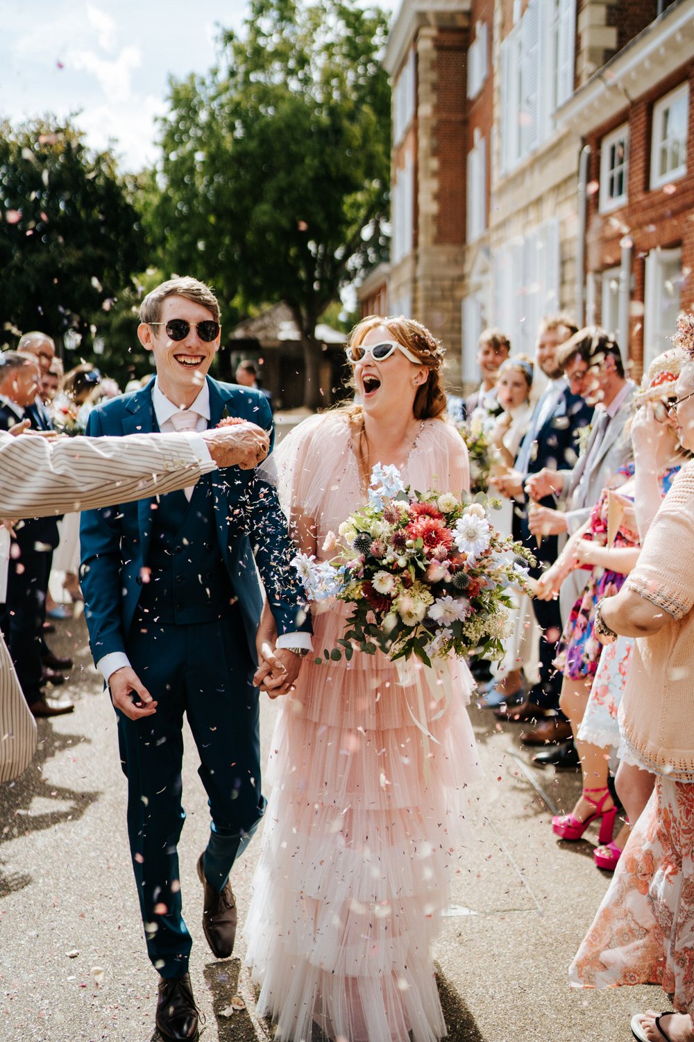 Bride and groom, wearing fashionable shades, walk down confetti tunnel outside York House in London