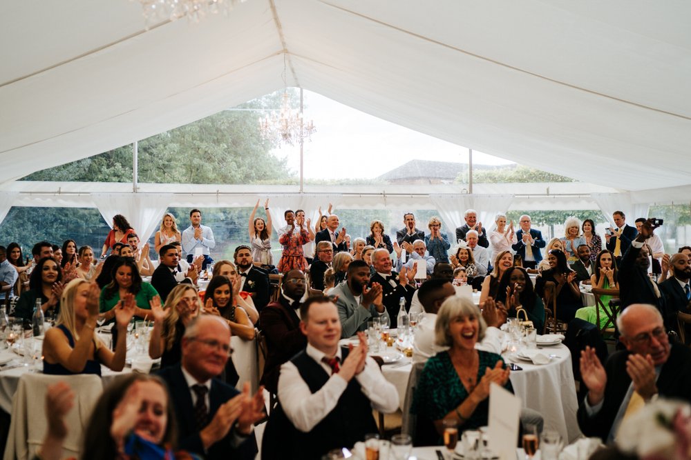 Wide photograph of a standing ovation during marquee wedding