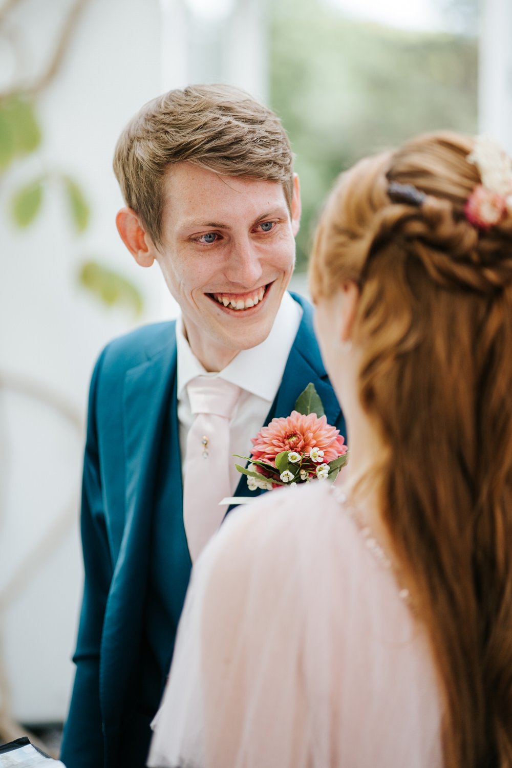 Groom, in elegant blue suit, looks lovingly at bride as wedding ceremony in York House begins