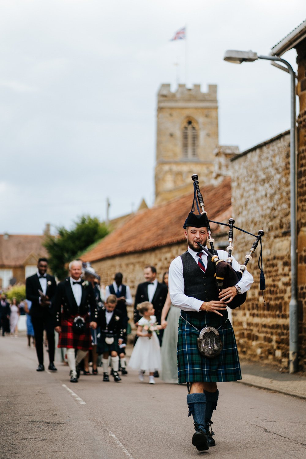 Traditional bagpiper leads procession of guests to wedding venue in Little Houghton