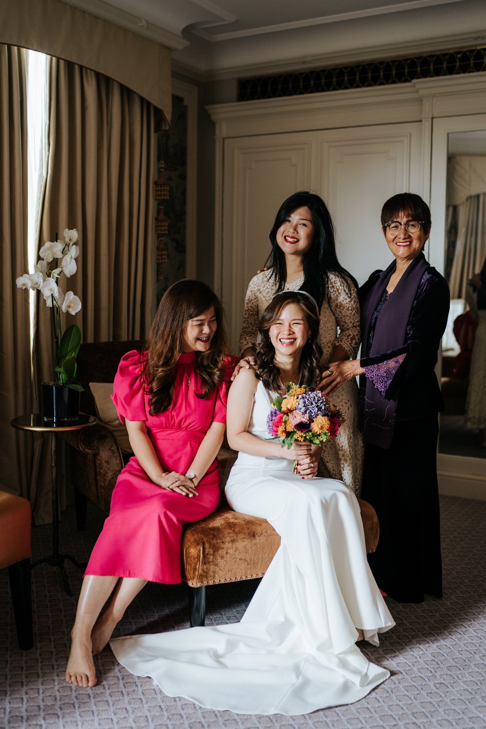 Bride, surrounded by two sisters and mother pose for photograph in suite at The Dorchester